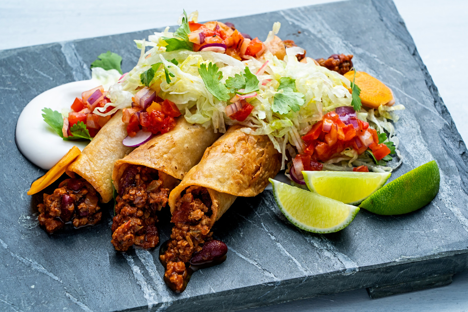 Vegan Chili Taquitos topped with greens, tomatoes, sour cream and limes